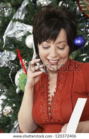 Happy middle aged woman communicating on mobile phone with Christmas tree in the background