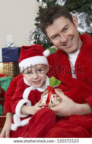Portrait of a happy Caucasian father and son in Santa Claus outfit holding gift