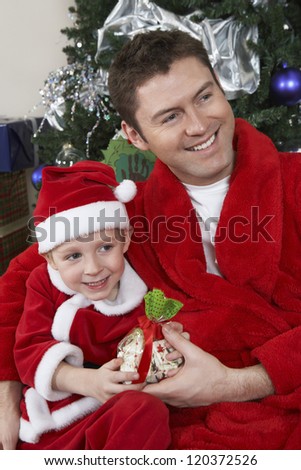 Happy Caucasian father and son in Santa Claus outfit holding gift