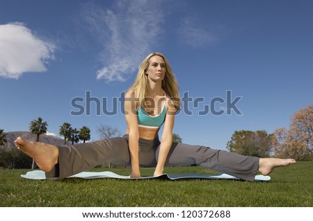 Young Caucasian woman performing yoga on mat at lawn