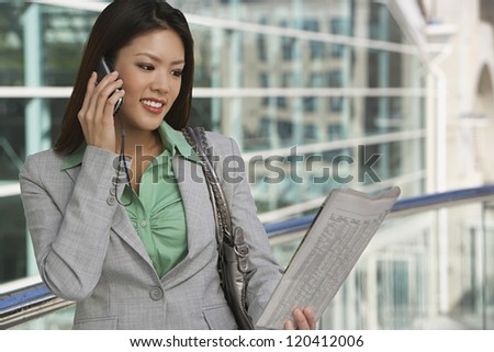Happy businesswoman on call reading newspaper in front of office building