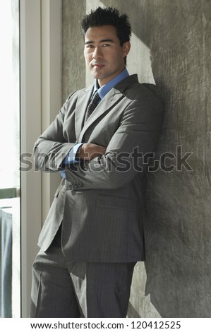 Portrait of handsome businessman with hands folded leaning on wall
