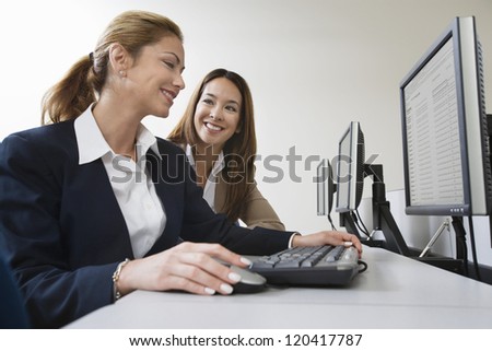 Happy business woman working on computer while colleague looking at her