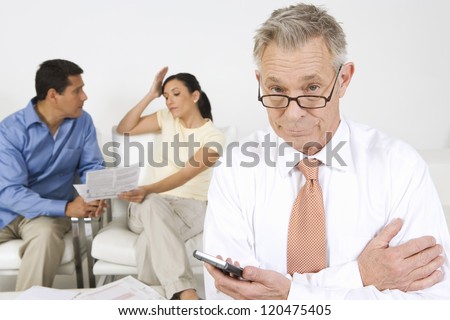 Senior financial adviser holding calculator with couple discussing in background