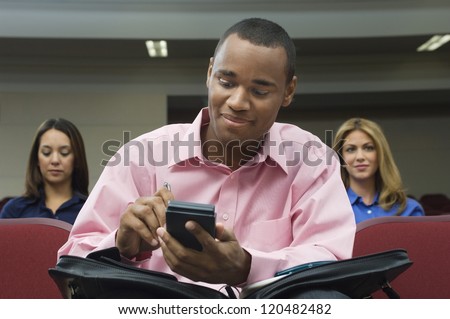An African American businessman using cell phone in class with colleagues in the background