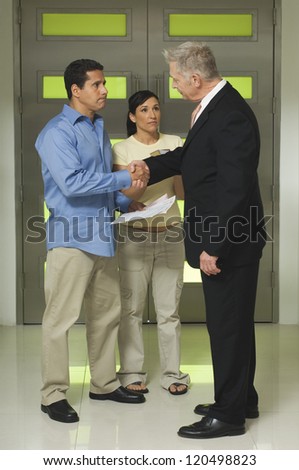 Full length of woman with man holding documents while shaking hand with senior businessman
