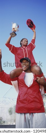 Low angle view cheerful African American baseball players with trophy against clear sky
