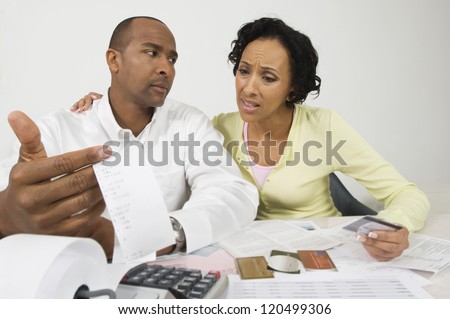 An African American worried couple with expense receipt and credit cards at home