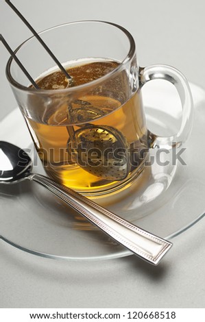 Closeup of a tea strainer dipped in cup filled with water over grey background