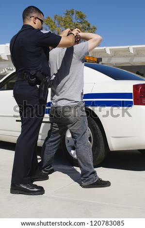 Police officer arresting young man by police car