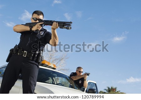 Police officer aiming with gun by car