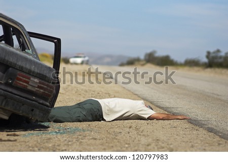 Injured man lying down on street by broken car