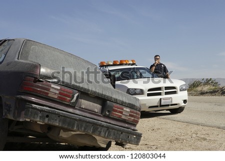 Police officer talking on radio watching abandoned car at roadside