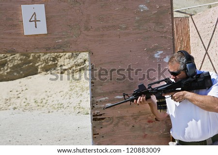 Mature man aiming with gun at combat training