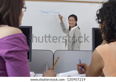 Mature professor writing on white board with two female students at classroom