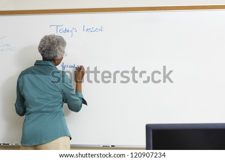 Rear view of a mature teacher writing on whiteboard at classroom