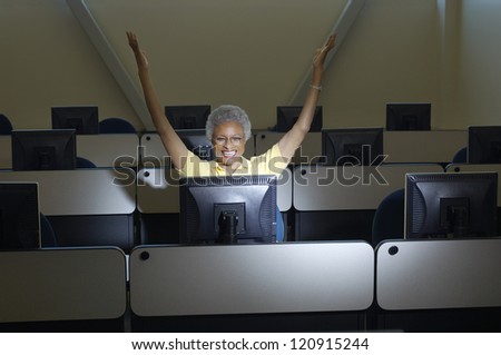 Happy senior woman raising hands in classroom