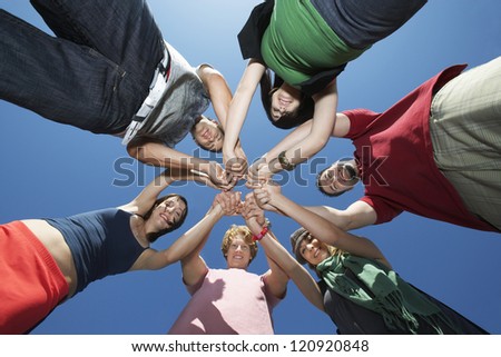 Low angle view of friends holding hands against blue sky