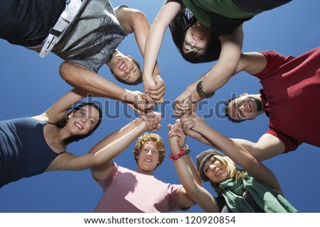 Low angle view of friends holding hands against blue sky