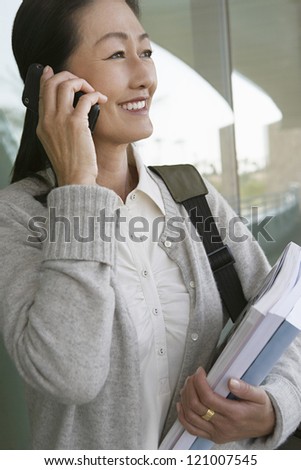 Side view of mature female teacher holding books while talking on phone