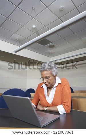 Senior teacher working on laptop in empty classroom