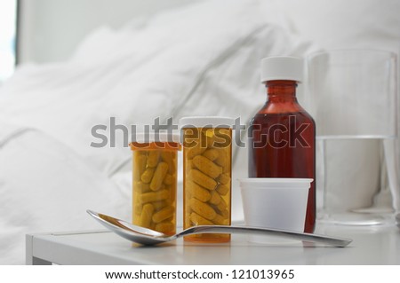 Cough syrup with spoon and pills beside bed at home