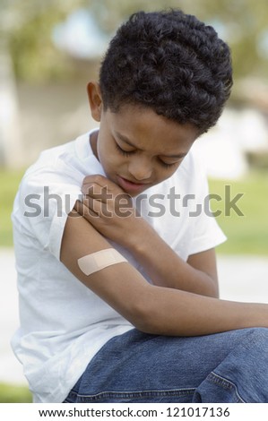 Sad African American boy looking at band aid on his arm