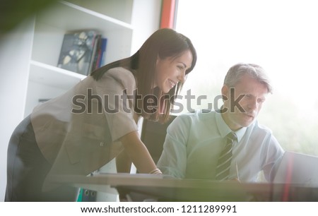 Senior male employee showing female employee numbers on his laptop pointing screen, this could be in a small business or even at home in the home office.