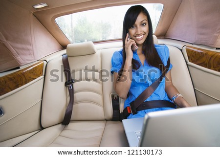 Portrait of an Indian business woman using laptop while communicating on cell phone in car