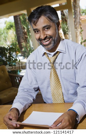 Portrait of a happy Indian businessman holding paper while sitting by table