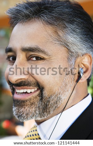 Closeup portrait of a happy Indian businessman listening music through headphone