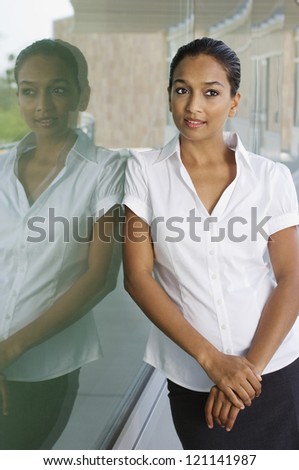Beautiful Indian business woman contemplating while leaning on glass