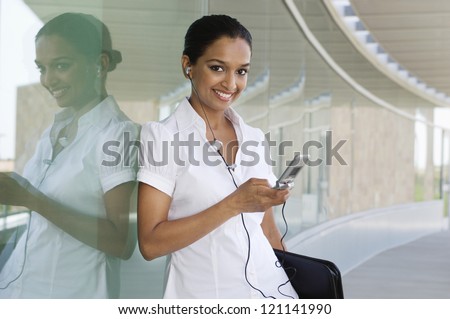 Portrait of a happy Indian business woman listening music on cell phone