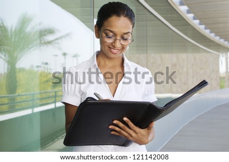 Happy Indian business woman writing notes in the folder at balcony