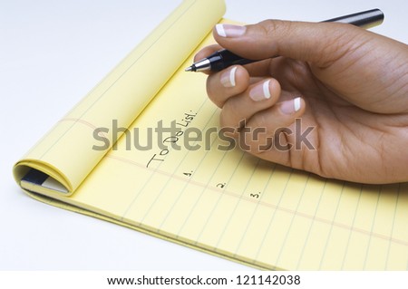 Closeup of woman with pen scheduling task list on notepad over white background