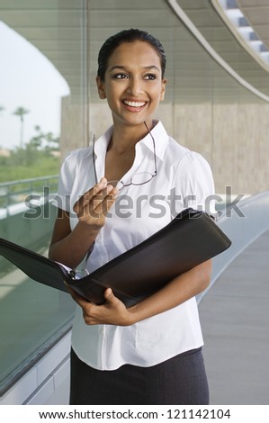 Happy Indian business woman holding folder and looking away