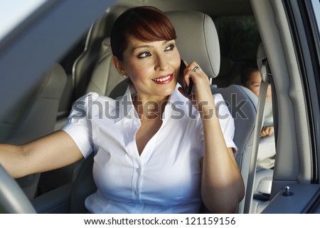 Happy business woman communicating on cell phone with son sitting on backseat