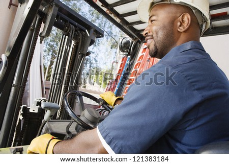 A happy African American  industrial worker driving forklift at workplace