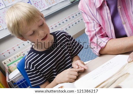 A preadolescent boy reading a book with his teacher in the classroom