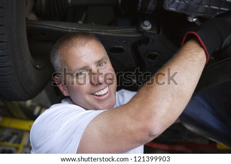 Portrait of a happy male mechanic repairing a lifted car