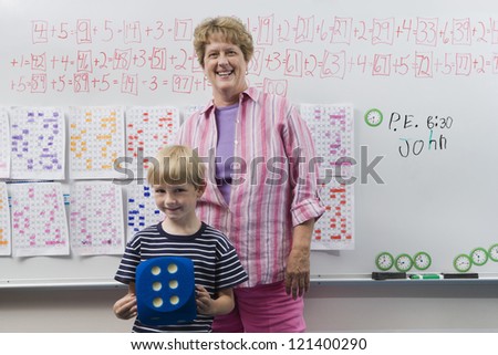 Portrait of a happy mature female teacher standing with her student against whiteboard