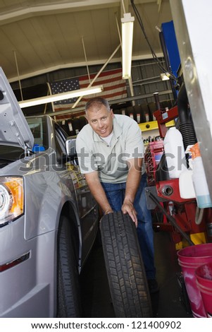 Portrait of a male mechanic changing spare car tire at workshop