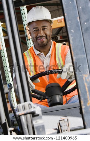 Portrait of a happy  male industrial worker driving forklift at workplace