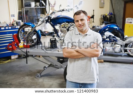 Portrait of a happy  male mechanic standing with hands folded at workshop