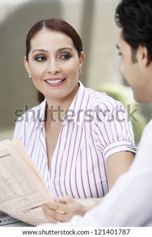 Happy beautiful business woman holding newspaper while looking at colleague