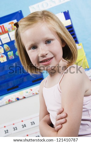 Portrait of a cute little girl with arms crossed standing in classroom