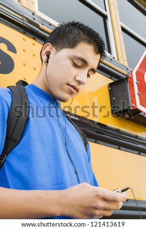 Handsome young man listening music against school bus