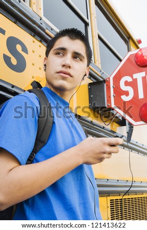 Handsome young man listening music against school bus with stop sign