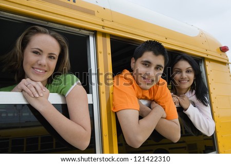 Portrait of young multiethnic students looking out from windows of a yellow school bus
