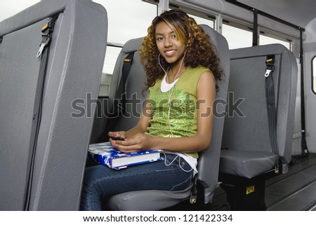 Portrait of young female student listening music on MP3 in school bus